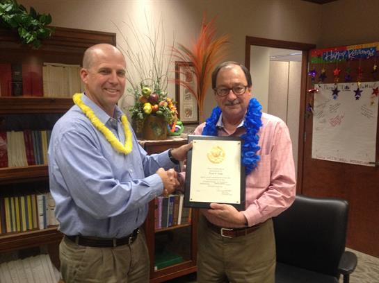 Two men are smiling as they celebrate an achievement in an office setting adorned with leis.