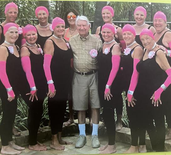 Women in black swimsuits and pink accessories relax outdoors with an older man.