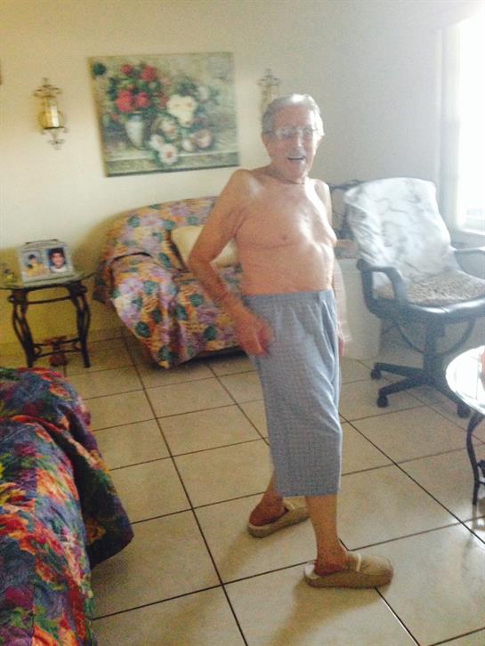 An elderly man with a friendly demeanor stands in a cozy living room wearing relaxed attire.