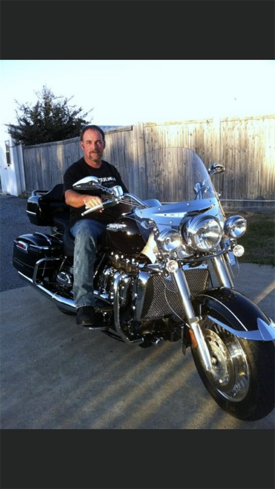 A man proudly sits on his motorcycle in a quiet neighborhood, enjoying the evening light.