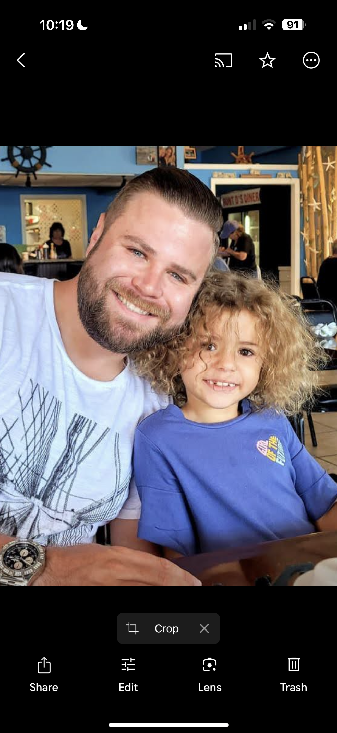 A happy father and his curly-haired son smile together while enjoying their time at a cafe.