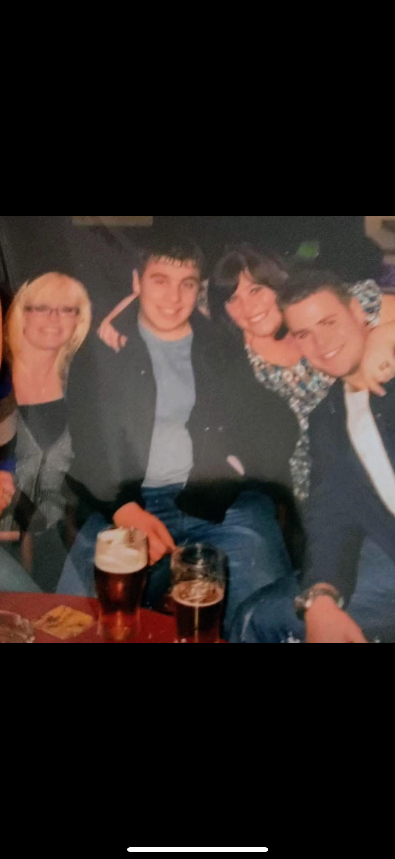 Five friends enjoy drinks and engage in lively conversation at a warm pub setting.