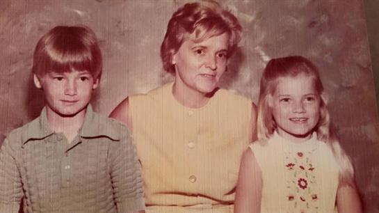 A mother smiles between her son and daughter against a vintage textured backdrop.