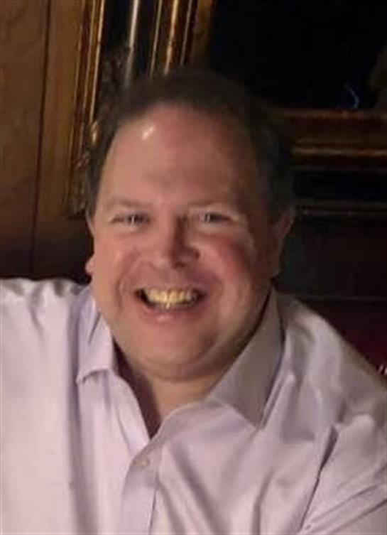 A joyful man with a bright smile interacts at a social gathering in a warm atmosphere.