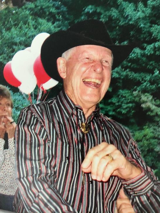 An elderly man in a cowboy hat laughs joyfully outdoors amidst colorful balloons.
