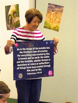 An older woman holds a sign discussing creation and faith at a community church event.