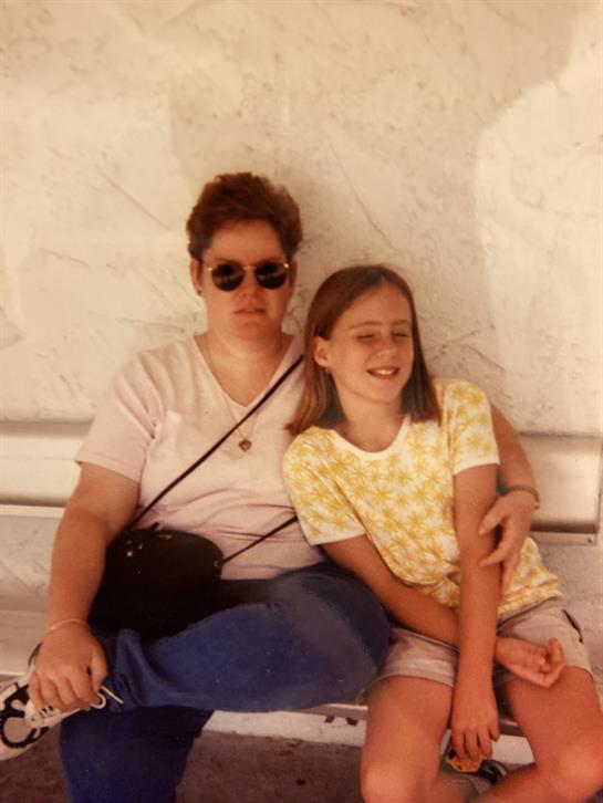 Two individuals sit close together, smiling while enjoying a sunny day outdoors.