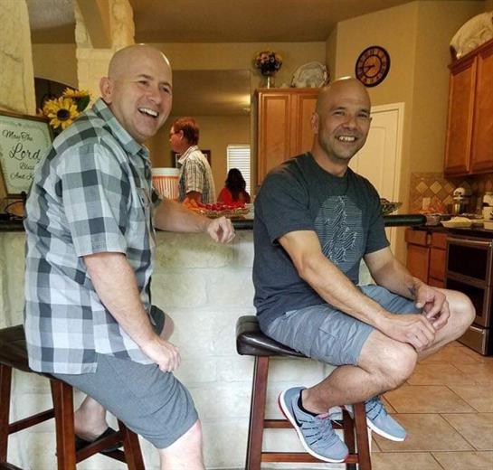 Two friends sit on stools, smiling and chatting in a warm, inviting kitchen setting.