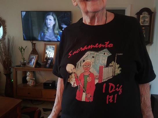 Elderly person smiles while showing off a playful t-shirt in a cozy home setting.