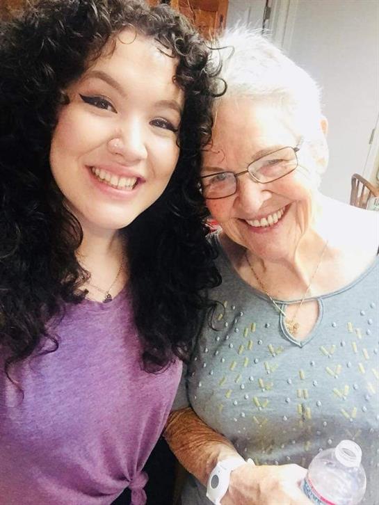 Two women smile happily at the camera, celebrating their bond in a cozy indoor space.