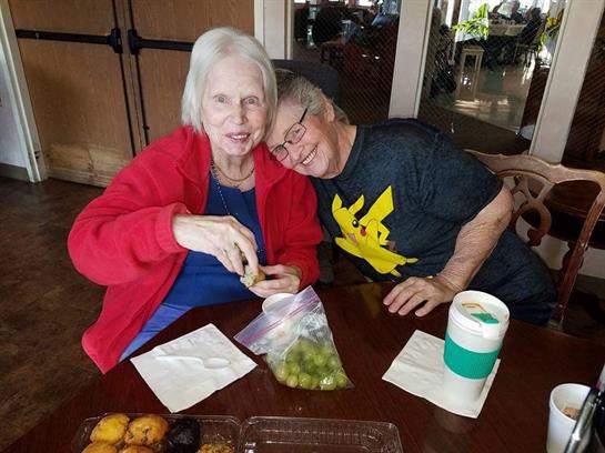 Two older women share grapes and enjoy each other's company at a cafe table.