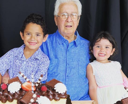 Grandchildren excitedly pose with their grandfather at a joyful birthday gathering, enjoying cake.