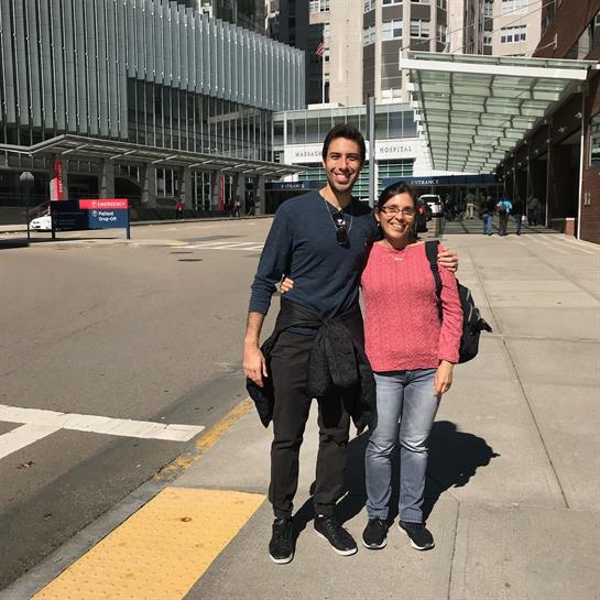 Two friends stand smiling on a city street, enjoying a warm sunny day with urban architecture.