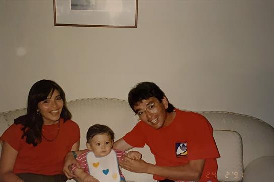 Two happy parents hold their baby in a warm and inviting living room while enjoying family time.