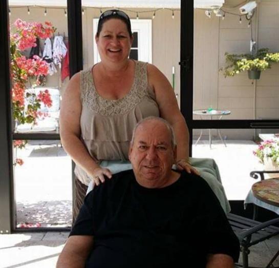A joyful woman stands behind a seated man, enjoying their time in a vibrant outdoor space.