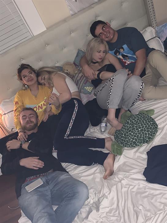 A group of friends is lounging on a bed, enjoying each other's company and a relaxed atmosphere.