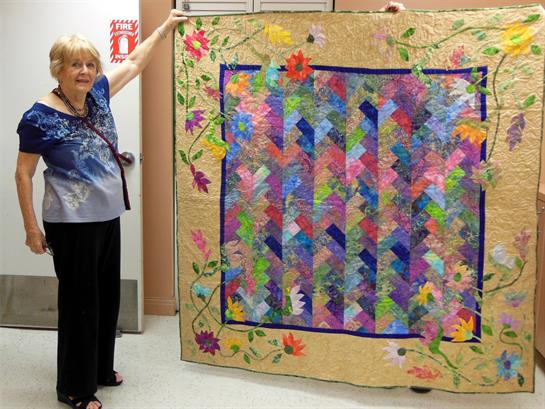 A senior woman displays a vibrant quilt with intricate patterns at the craft fair.