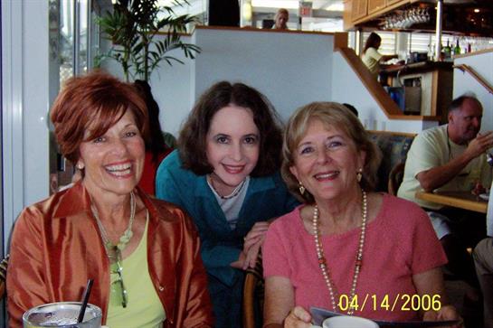 Three women share a joyful moment, smiling and interacting in a lively cafe.