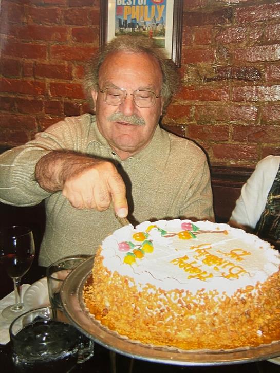 A man cuts a decorated cake surrounded by friends and warm restaurant ambiance.