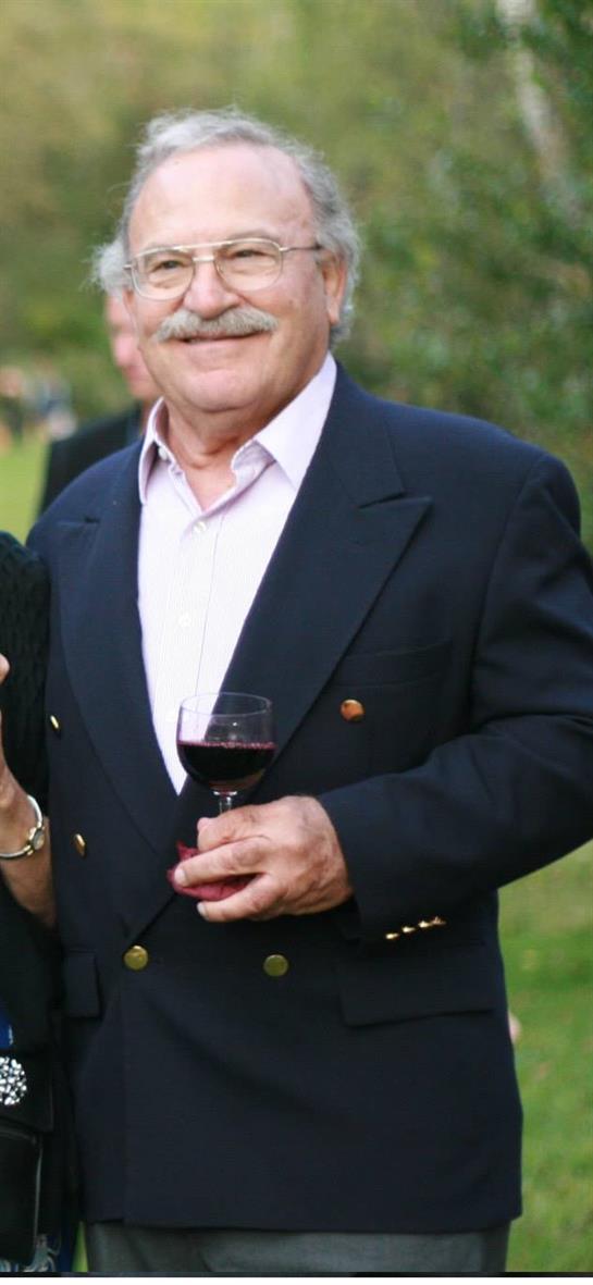 Group of friends celebrates in a garden, with an elderly man holding wine and smiling happily.