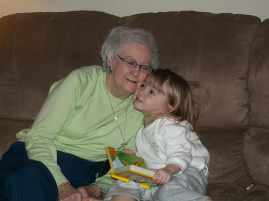 A cheerful grandmother embraces her playful granddaughter while sitting on a couch at home.