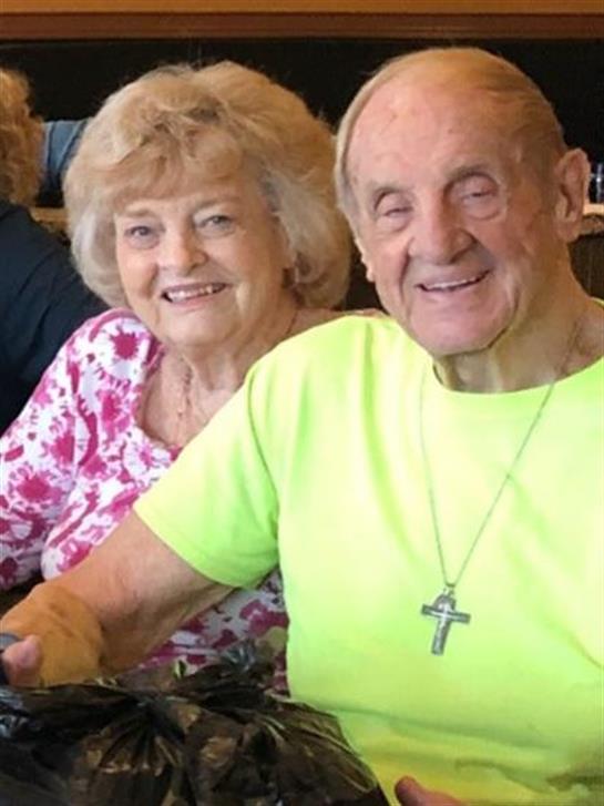 Two seniors share a joyful moment while enjoying lunch at a restaurant filled with friends.