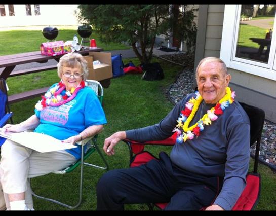 Elderly couple relaxes in the sun, wearing colorful leis in their backyard.