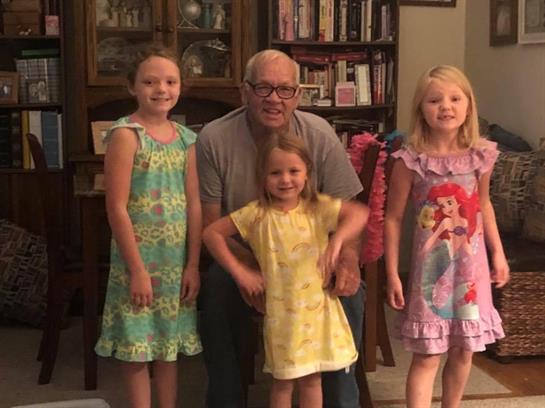 A grandfather is surrounded by his four granddaughters, joyfully posing together at home.