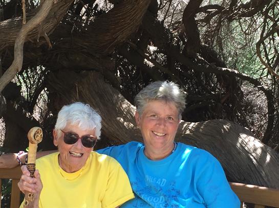 Two women sit together, laughing and enjoying each other's company in a natural environment.
