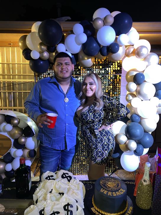 Two people share a joyful moment at a celebration with balloons and drinks.