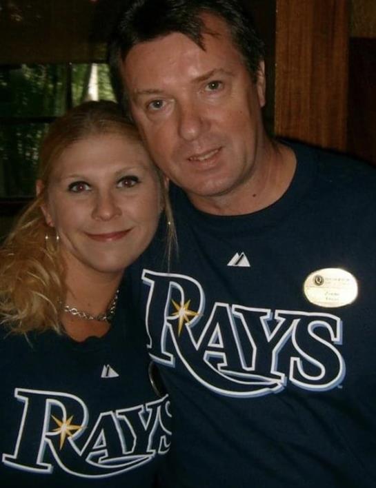 Two fans are smiling while wearing matching team shirts in a relaxed atmosphere.