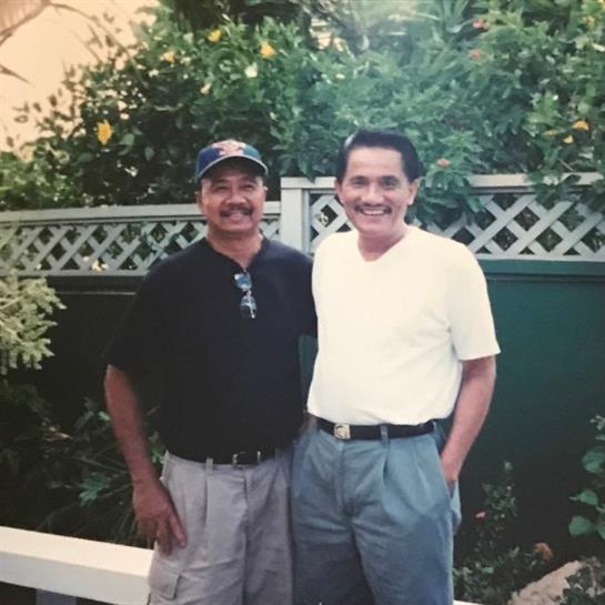 Two men smile together in a vibrant garden, enjoying a friendly moment under the sun.