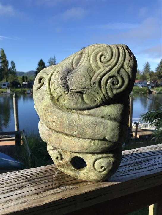 Intricately carved stone sits on a railing by a serene lake under clear blue skies.