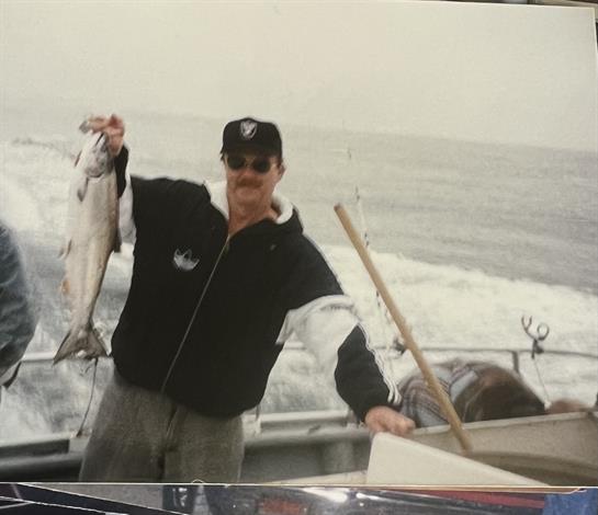Man proudly shows off a large fish while fishing from a boat in cool, cloudy weather.