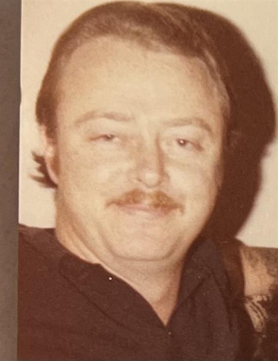 A friendly man smiles softly in a relaxed indoor setting, capturing a joyful moment.