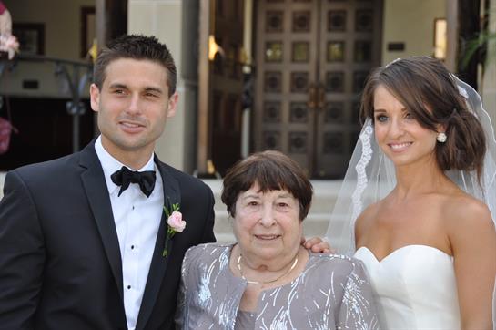 Newlyweds pose with a cherished relative at their wedding venue on a sunny day