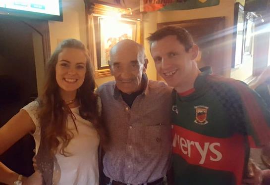 Three individuals smile together in a cozy pub setting, enjoying a festive evening.