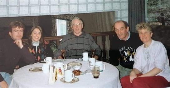 Three elderly friends share stories and laughter at a table filled with coffee and treats.