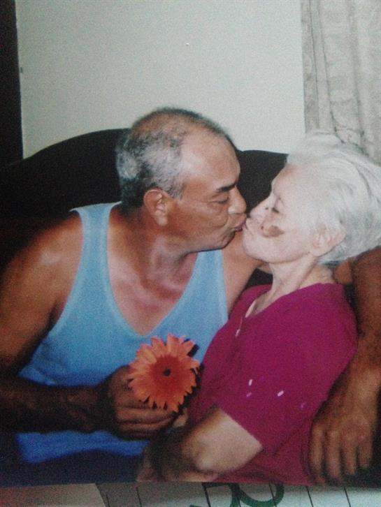 An older couple enjoys a sweet kiss on the couch in their cozy living room, surrounded by warmth.