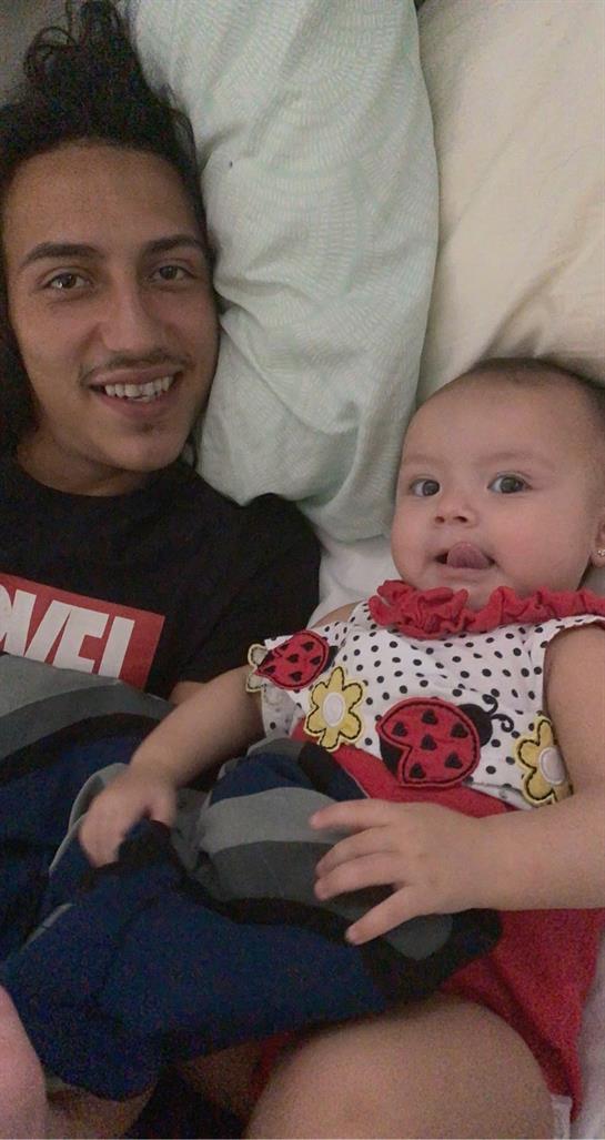 A father snuggles with his baby, both smiling happily while relaxing on a bed together.