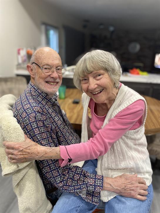 Two seniors share a joyful moment, smiling and embracing during a cozy afternoon at home.