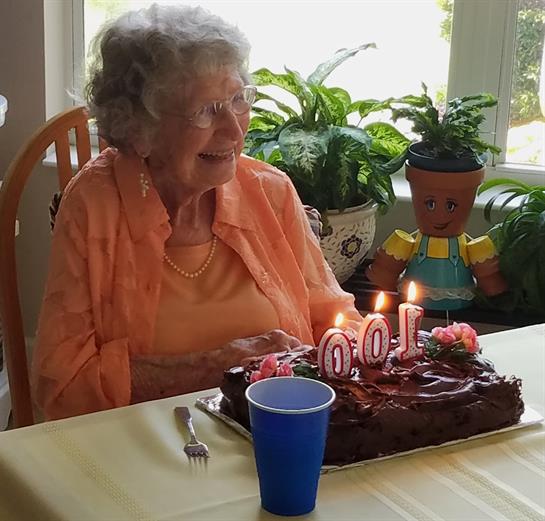 An elderly woman joyfully celebrates her birthday surrounded by a cake, candles, and family.