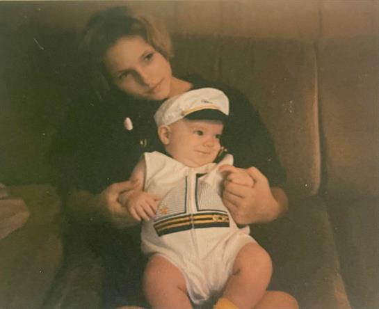 A mother lovingly holds her baby in a sailor outfit, both radiating warmth in a cozy setting.