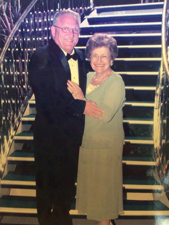 Elderly couple smiles warmly while posing together on elegant staircase during a formal gathering.