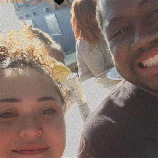 Two friends smile, celebrating outdoors with drinks in the warm sunshine.