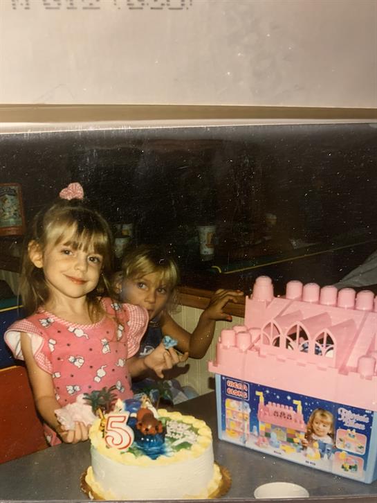 Two girls enjoy a birthday celebration featuring a pink cake and a toy castle nearby.