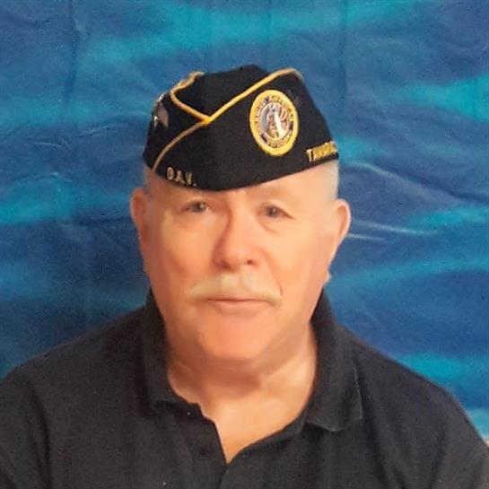 A veteran in a military cap stands confidently against a bright blue backdrop.