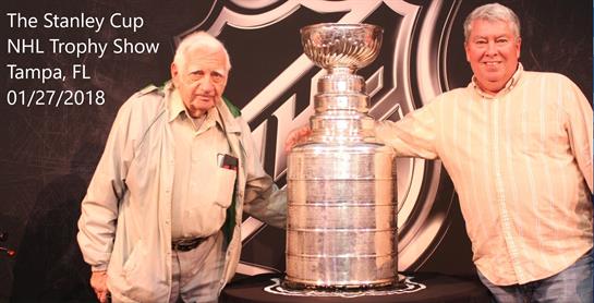 Two individuals proudly stand beside a large silver trophy at a memorable sports gathering.