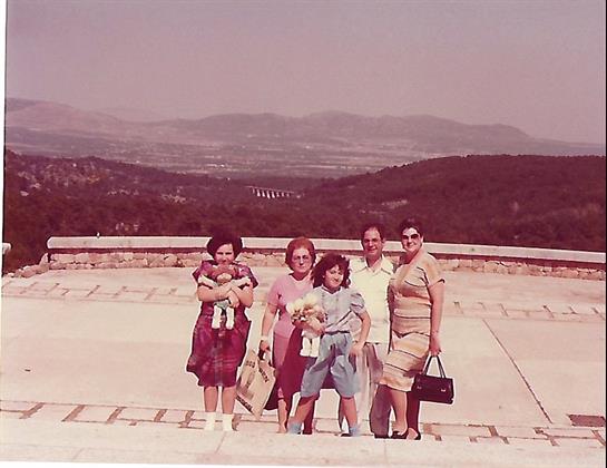 Six family members pose happily together near a scenic viewpoint, enjoying a sunny day outside.