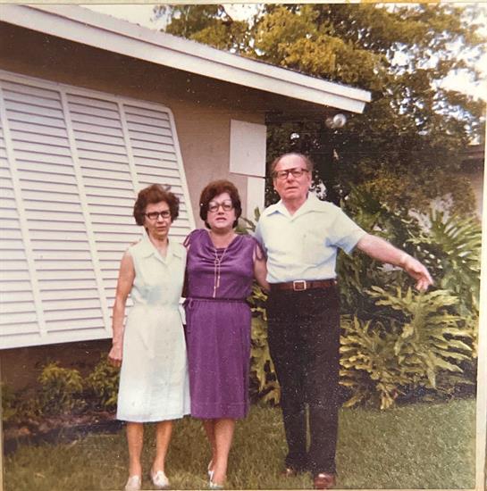 Three friends stand together in a lush garden outside a house, enjoying a sunny day.